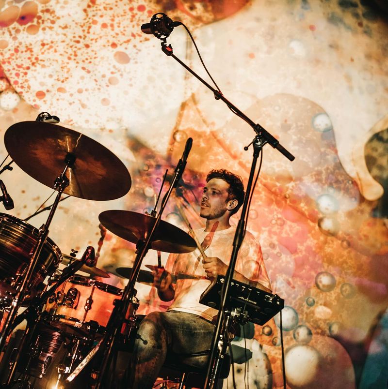 Drummer behind his kit in a wash of projected colour